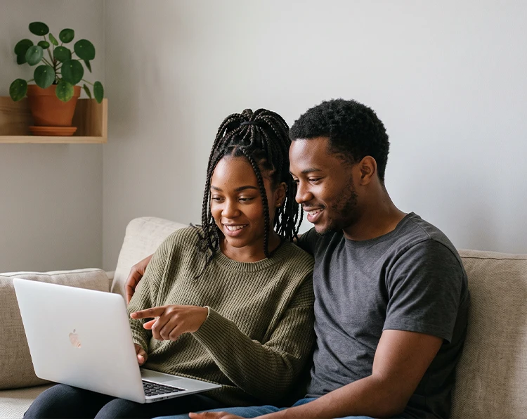 A happy couple sitting on the couch at home while looking for cash loan options using a laptop