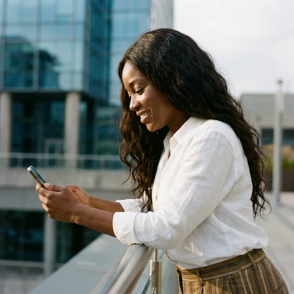 a stylish Black woman in profile, looking down and smiling warmly at her smartphone